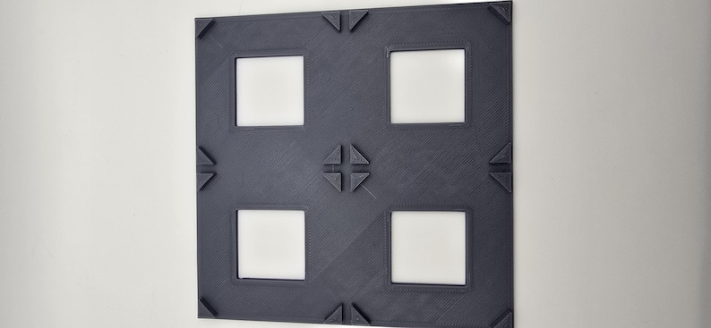May include: A dark gray picture frame with four square openings. The frame has a decorative design with a cross in the center and triangles at the corners.