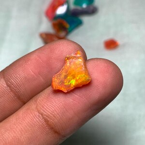 May include: A small, rough, orange and green opal gemstone with iridescent flashes of color.