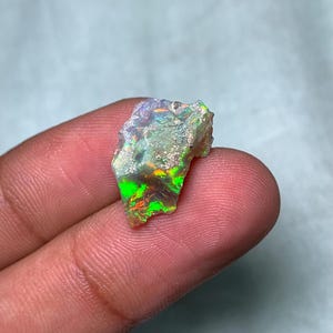 May include: A rough, natural opal gemstone with a milky white base and flashes of green, orange, and purple.