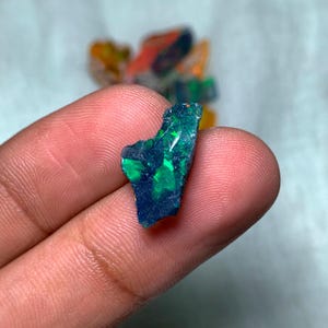 May include: A rough, dark blue and green opal gemstone with iridescent flashes of color.
