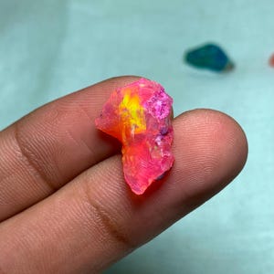 May include: A small, irregularly shaped piece of pink and yellow opal with a rough, textured surface.