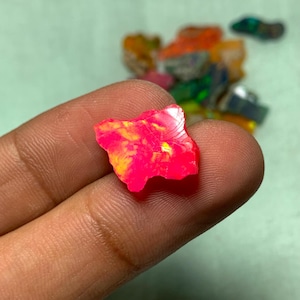 May include: A pink and yellow opal gemstone with a rough, irregular shape. The gemstone is held in a hand.