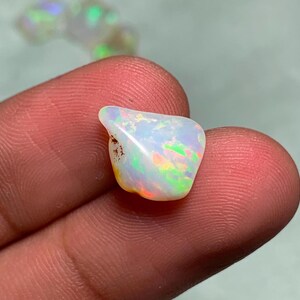 May include: A white opal gemstone with iridescent rainbow colors. The opal is irregularly shaped and has a rough, natural finish.