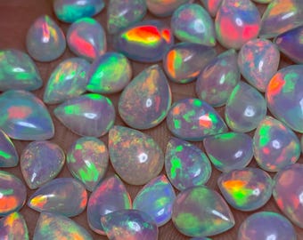 May include: A collection of iridescent opal teardrop cabochons in various shades of white, pink, green, and blue. The opals are smooth and polished, with a pearlescent sheen.