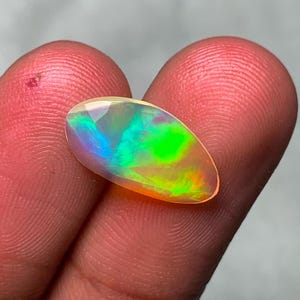 May include: A vibrant, oval-shaped opal gemstone with a rainbow of colors, including green, blue, and orange.