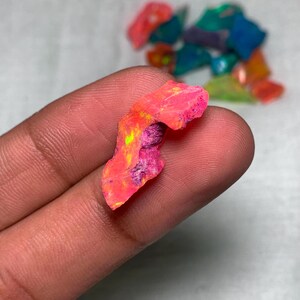 May include: A pink, green, and yellow opal gemstone with a rough, irregular shape. The opal is translucent and has a vibrant iridescent sheen.