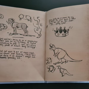 May include: A page from a journal with black ink drawings of a ram, a dinosaur, and a crown. The text on the page reads "Joel said he's taking me on a camping trip next week for my birthday. Found something he says I'll love! He's acting very proud of himself. Smug old fogey." and "Dina made me a crown for my birthday. She went back to that camp and got all this paper... it's pretty great."