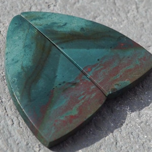 May include: Two pieces of green and red jasper, a type of semi-precious stone, with a unique swirling pattern. The pieces are cut in a triangular shape with rounded edges.