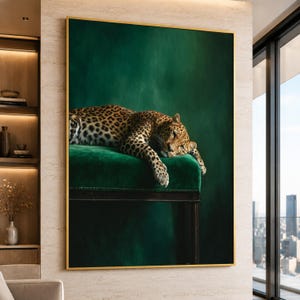 May include: A large rectangular wall art print featuring a leopard with a spotted coat resting on a plush, deep green velvet bench. The leopard is positioned horizontally, with its head and front paws draped over the edge of the seat. The background is a solid, dark emerald green, and the entire artwork is encased in a thin, metallic gold frame.