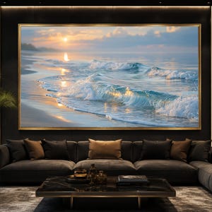May include: A large rectangular wall art piece featuring a sunset over a beach with rolling ocean waves. The scene displays golden sunlight reflecting on the water and wet sand, framed in a thin gold border, mounted above a dark grey sofa.