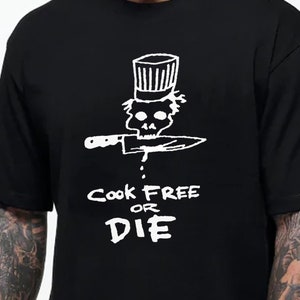 以下が含まれることがあります： 白いシェフの帽子をかぶってナイフを持った骸骨の白いグラフィックがプリントされた黒いTシャツ。グラフィックの下に「Cook Free or Die」というテキストが書かれています。