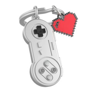 Könnte beinhalten: Ein silberfarbener Schlüsselanhänger mit einem Videospiel-Controller-Design mit einem schwarzen Steuerkreuz und Knöpfen. Ein roter, pixeliger Herzanhänger hängt an dem Schlüsselanhänger. Der Schlüsselanhänger ist einem klassischen Videospiel-Controller nachempfunden.