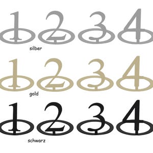 Könnte beinhalten: Satz von zwölf Tischnummern-Platzkarte-Haltern in drei Farben: Silber, Gold und Schwarz. Jede Nummer wird in einer stilisierten Schriftart angezeigt und ist an einer runden Basis befestigt.