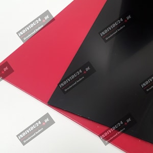 Könnte beinhalten: Zwei Blätter aus Kunststoff, eines rot und eines schwarz, mit dem Text "INDIVIDU24 DE Gravierend Anders" auf jedem Blatt.