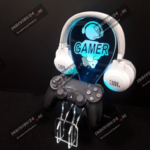 Könnte beinhalten: Ein blauer Acryl-Ständer mit einem Gamer-Logo und einem Headset-Halter. Ein schwarzer Videospiel-Controller befindet sich auf dem Ständer. Der Ständer ist mit blauen LED-Lichtern beleuchtet.