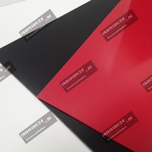 Könnte beinhalten: Nahaufnahme von drei Acrylglasscheiben in Schwarz, Weiß und Rot. Die Platten liegen übereinander. Der Text "INDIVIDU24 DE Gravierend Anders" ist auf jeder Platte aufgedruckt.