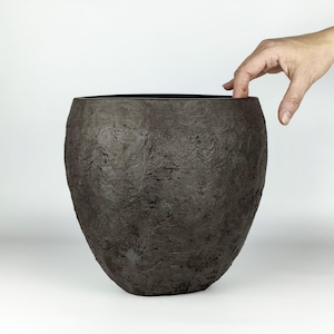 May include: A dark brown, rounded planter with a heavily textured, rough surface. The vessel features a wide, open top and a tapered base, showcasing a deep, earthy tone and a rugged, uneven exterior finish that provides a distinct tactile appearance.