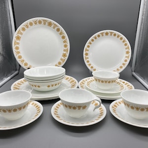 Pode incluir: Um conjunto de jantar branco com um padrão floral dourado. O conjunto inclui pratos, tigelas, pires e chávenas de chá. Os pratos medem aproximadamente 25 cm de diâmetro.
