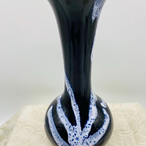 Puede incluir: Un jarrón de cerámica negro con base bulbosa y parte superior acampanada. Patrones blancos, abstractos y verticales decoran el jarrón. El jarrón se exhibe sobre una superficie texturizada de color crema.