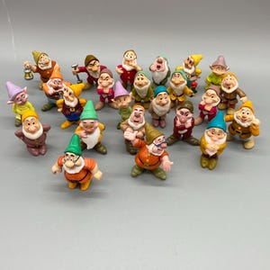 Pode incluir: Uma coleção de vinte e duas pequenas figuras de plástico pintado representando vários personagens anões. Cada figura usa um chapéu, túnica e calças de cores distintas, com diversas expressões faciais e poses variadas.