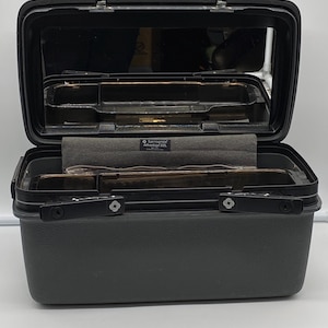 May include: Open black Samsonite Advantage SSL vanity case with a mirror, interior compartments, and a gray fabric lining. The case is made of a durable, textured material and has a handle for easy carrying. The case is designed for travel and storage.