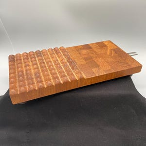 May include: A rectangular wooden cutting board featuring two distinct surface textures. One half displays a grid of raised pyramid-shaped points, while the other half consists of a smooth, flat end-grain pattern with visible wood grain variations.