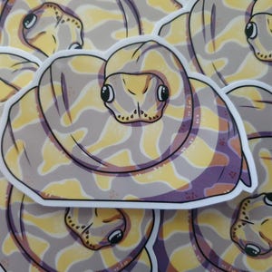 May include: A pile of stickers depicting a cartoon snake in a coiled pose. The snake is patterned with yellow, purple, and grey, and has large eyes. Each sticker has a white border.