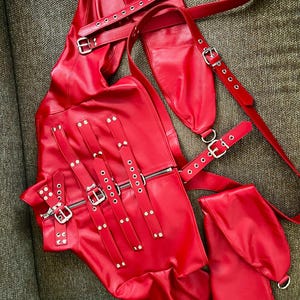 May include: Red leather jacket with multiple straps and buckles. The jacket has a zip fastening and is decorated with silver studs.