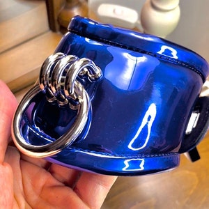 May include: A blue leather cuff with a silver metal ring. The cuff is shiny and has a smooth surface.
