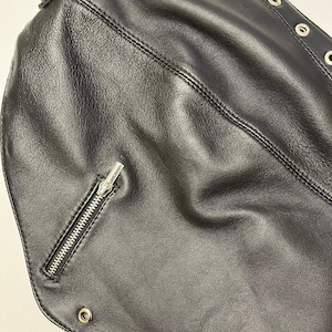 May include: Close-up of a black leather accessory with a zipper and metal grommets. The accessory has a textured surface and is stitched with a visible seam. Silver-colored metal spikes are visible at the bottom.