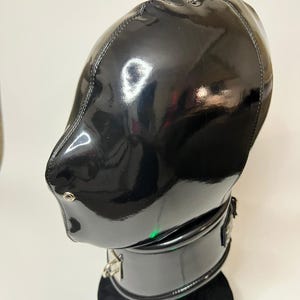 Peut inclure: Un capuchon noir brillant avec un anneau métallique sur le dessus. Le capuchon a une fermeture éclair et un col. Le matériau semble être du cuir verni ou un matériau brillant similaire. Le capuchon est conçu pour couvrir la tête et le cou.