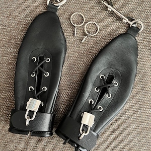 Pode incluir: Restrições de couro preto com ferragens prateadas. As restrições apresentam um design com atacadores e um fecho de fivela. Duas chaves e dois mosquetões de metal também estão incluídos.
