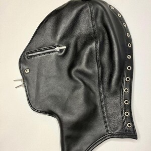 May include: Black leather hood with a zipper closure on the front and a row of metal grommets along the side. The hood is designed to cover the head and neck.