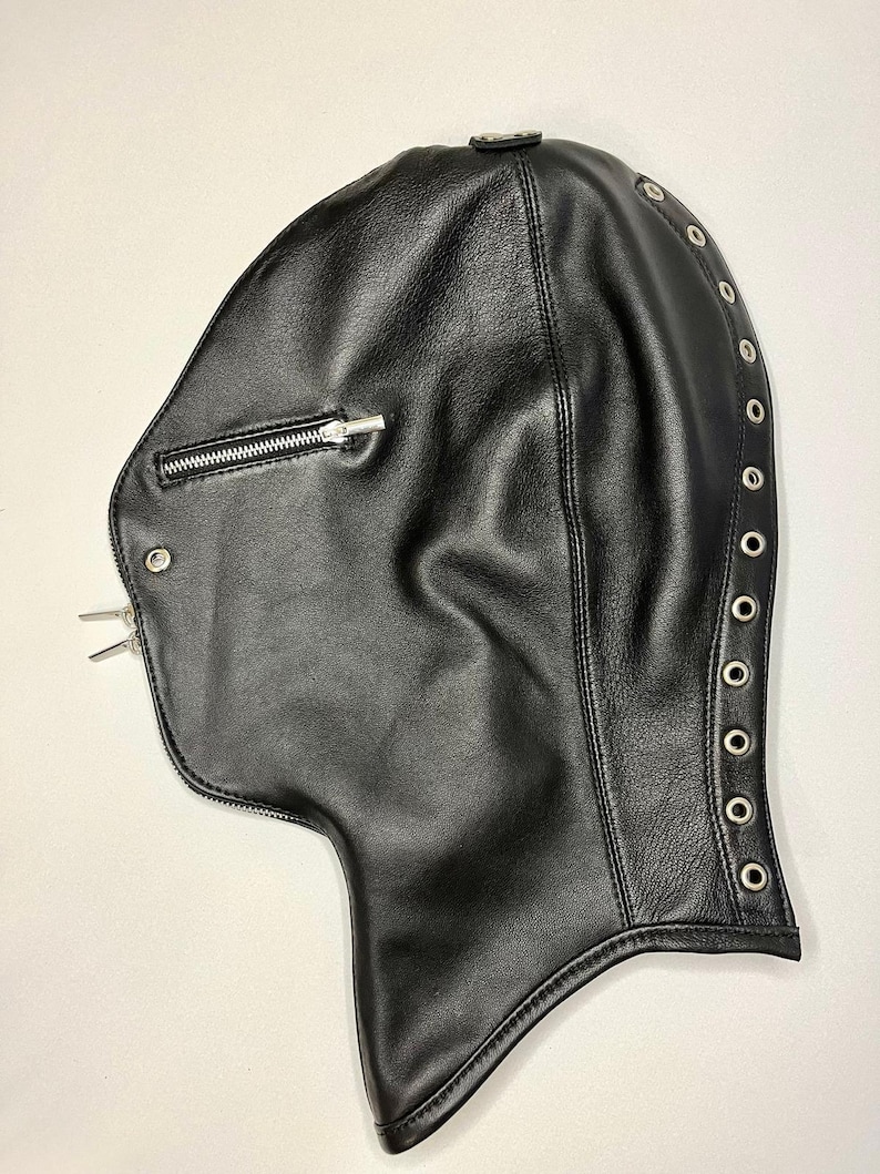 May include: Black leather hood with a zipper closure on the front and a row of metal grommets along the side. The hood is designed to cover the head and neck.