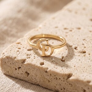 K&ouml;nnte beinhalten: Ein goldfarbener Ring mit einem zentralen Design aus den ineinandergreifenden Gro&szlig;buchstaben C und P. Der Ring ist d&uuml;nn und kreisf&ouml;rmig, wobei die Buchstaben in den oberen Teil des Rings integriert sind und eine durchgehende Metallform bilden.