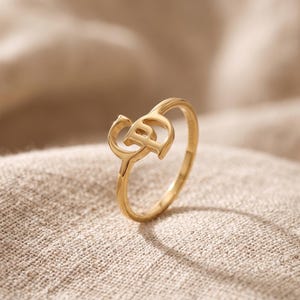 K&ouml;nnte beinhalten: Ein goldfarbener Ring mit polierter Oberfl&auml;che und einem zentralen Dekorelement in Form der ineinandergreifenden Buchstaben C und P. Der Ring ist d&uuml;nn und kreisf&ouml;rmig gestaltet und weist eine glatte, reflektierende Oberfl&auml;che auf.