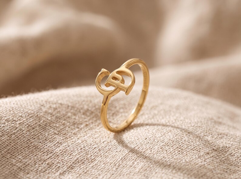 K&ouml;nnte beinhalten: Ein goldfarbener Ring mit polierter Oberfl&auml;che und einem zentralen Dekorelement in Form der ineinandergreifenden Buchstaben C und P. Der Ring ist d&uuml;nn und kreisf&ouml;rmig gestaltet und weist eine glatte, reflektierende Oberfl&auml;che auf.