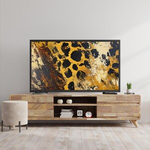 Puede incluir: Un mueble de TV de madera con un acabado de madera clara y tres estantes. Un televisor de pantalla plana con un marco negro est&aacute; en la parte superior del mueble. La pantalla del televisor muestra un primer plano de un patr&oacute;n de estampado de leopardo en tonos de amarillo, marr&oacute;n y negro.