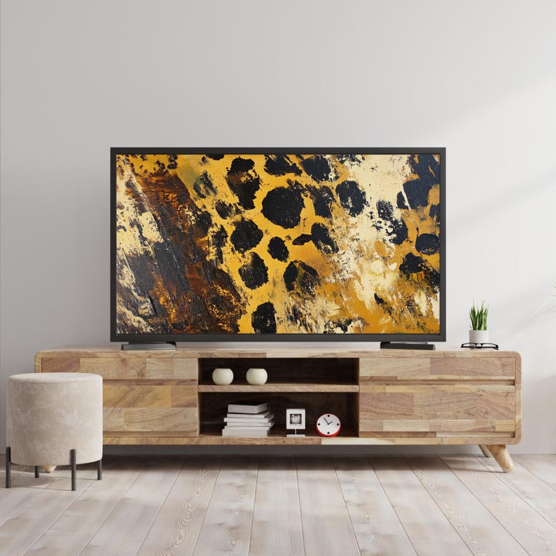 Puede incluir: Un mueble de TV de madera con un acabado de madera clara y tres estantes. Un televisor de pantalla plana con un marco negro est&aacute; en la parte superior del mueble. La pantalla del televisor muestra un primer plano de un patr&oacute;n de estampado de leopardo en tonos de amarillo, marr&oacute;n y negro.