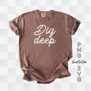 Op de afbeelding: Een bruin t-shirt met de woorden "Dig deep" in witte letters. Het shirt heeft een ronde hals en korte mouwen, met opgerolde mouwen. Het shirt is gemaakt van een zacht, comfortabel materiaal.