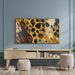 Puede incluir: Una consola de medios de madera con un caj&oacute;n y estantes, que presenta una pintura abstracta enmarcada de un patr&oacute;n de estampado de leopardo en tonos marrones, amarillos y negros. La consola est&aacute; en una habitaci&oacute;n con paredes de color azul claro y un suelo de madera clara.