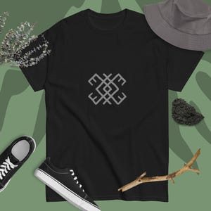 May include: Black t-shirt with a gray geometric design. The design is a stylized symbol with a square shape and four arms.