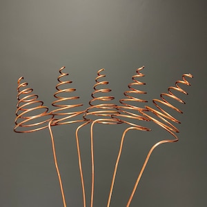 May include: Five copper wire spirals, each with a different number of coils, are arranged in a fan shape against a grey background. The spirals are attached to long, straight wires that extend downwards.