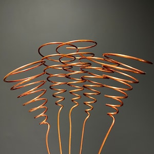 May include: Five copper wire spirals, each with a different number of coils, are arranged in a fan shape. The spirals are attached to straight wires that extend downwards.