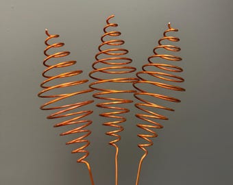 May include: Three copper-colored metal wire ornaments, each shaped into a tapered spiral cone. The wire coils are arranged vertically, with each spiral attached to a thin, straight metal stem extending downward from the base of the cone.