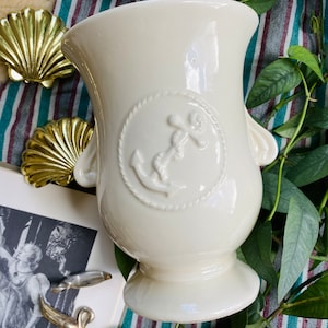 May include: White ceramic vase with a raised anchor design. The vase has two handles and a round base.
