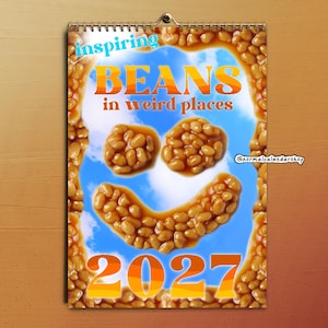 May include: A 2027 wall calendar featuring a border of baked beans and a central image of beans arranged into a smiley face against a blue sky background. The text reads inspiring BEANS in weird places and 2027, with a small normalcalendarshop logo.