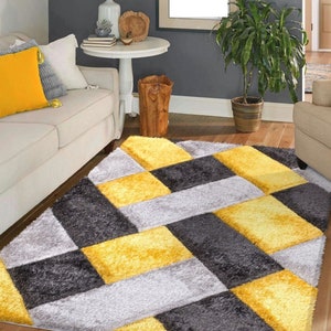 May include: A gray, yellow, and white geometric patterned area rug with a plush texture. The rug has a chevron pattern with squares.