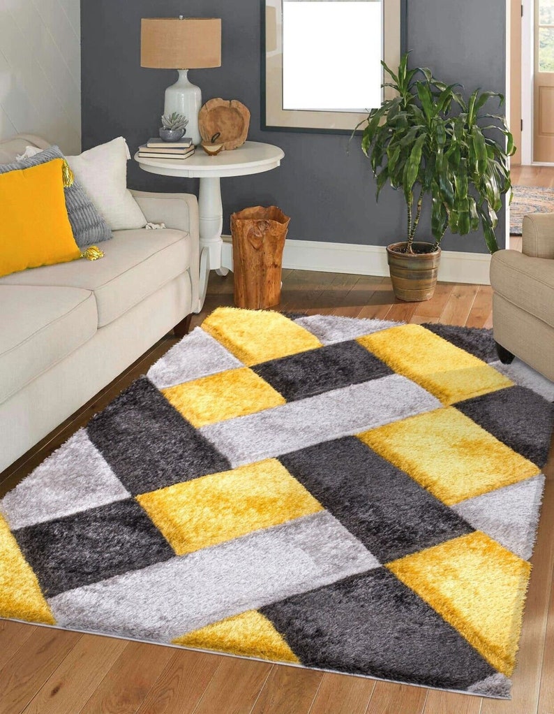 May include: A gray, yellow, and white geometric patterned area rug with a plush texture. The rug has a chevron pattern with squares.