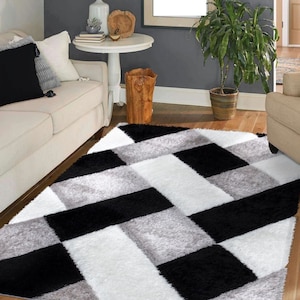 May include: A black and white geometric patterned rug with a shaggy texture. The rug is laid out on a hardwood floor in a living room setting.